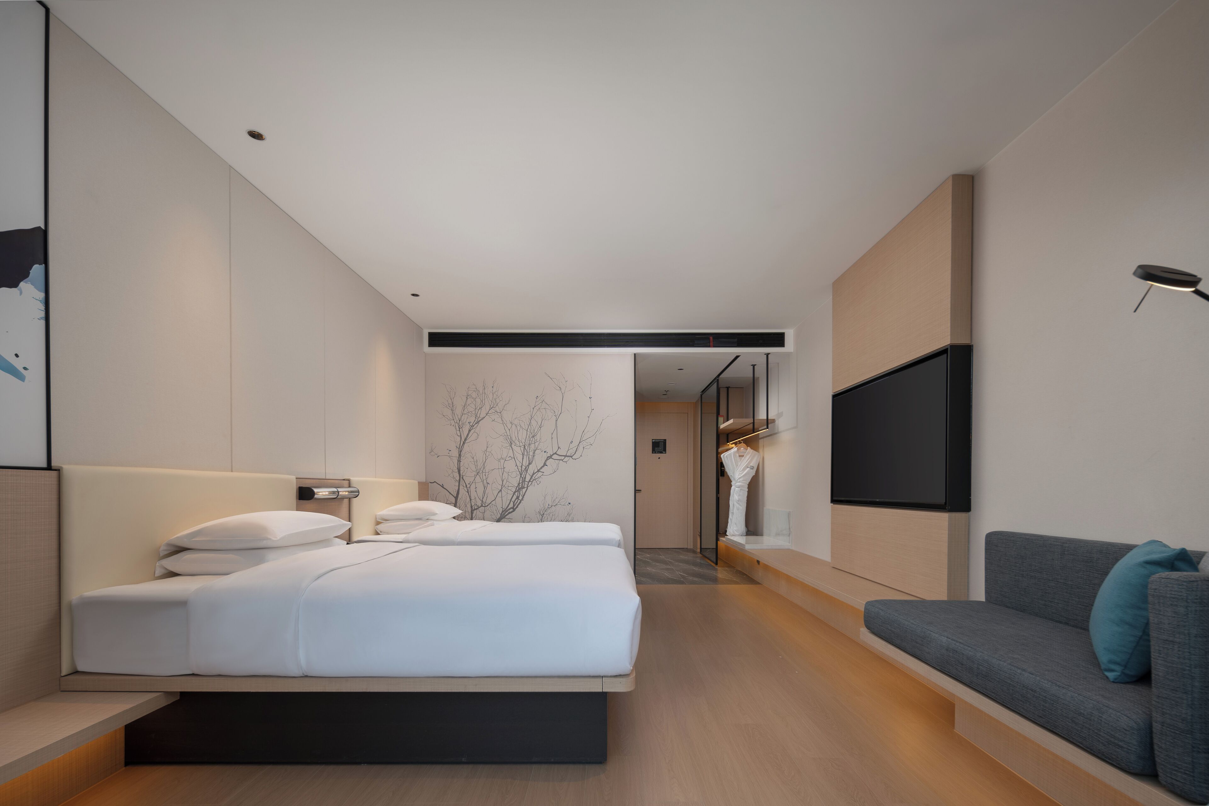 A modern hotel room with a large bed, a sofa, a flat-screen TV, and a minimalist decor.