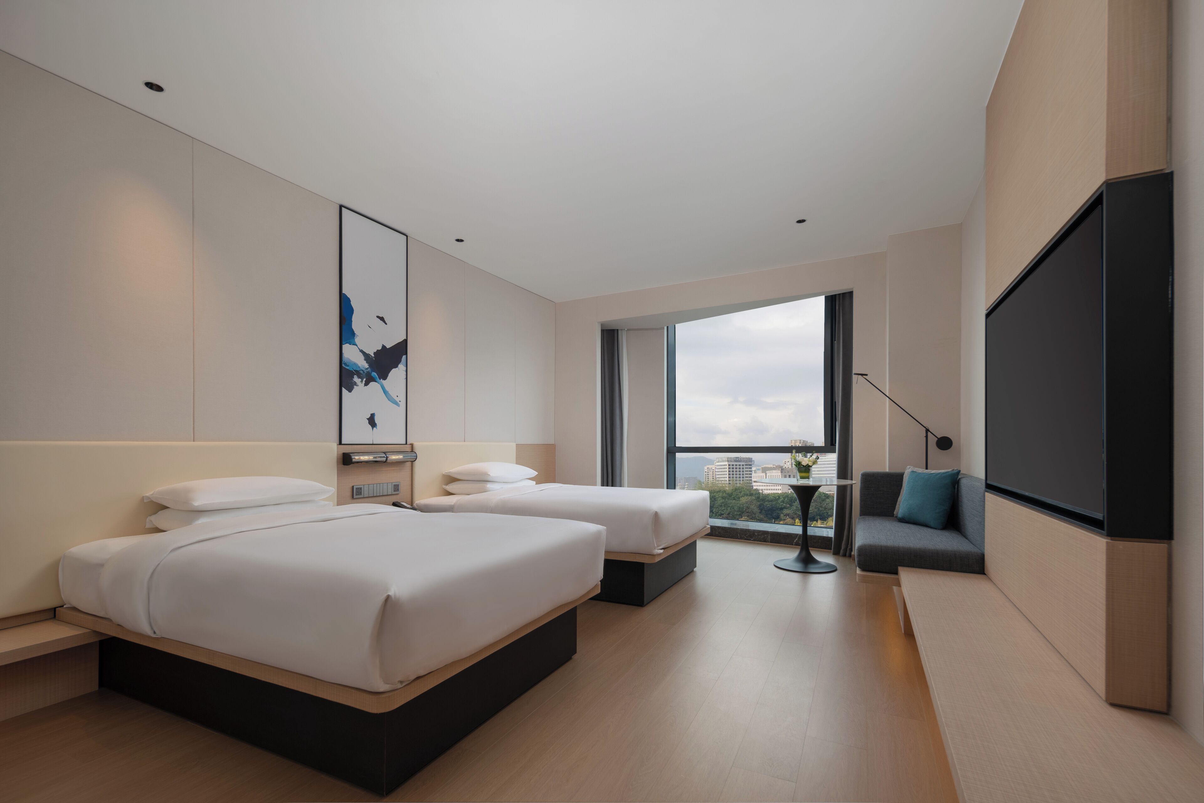 A modern hotel room with two beds, a large window, a sofa, and a TV.