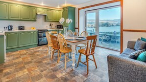 Una cocina con armarios verdes, una mesa de comedor con sillas y vistas a un lago a través de un ventanal grande.