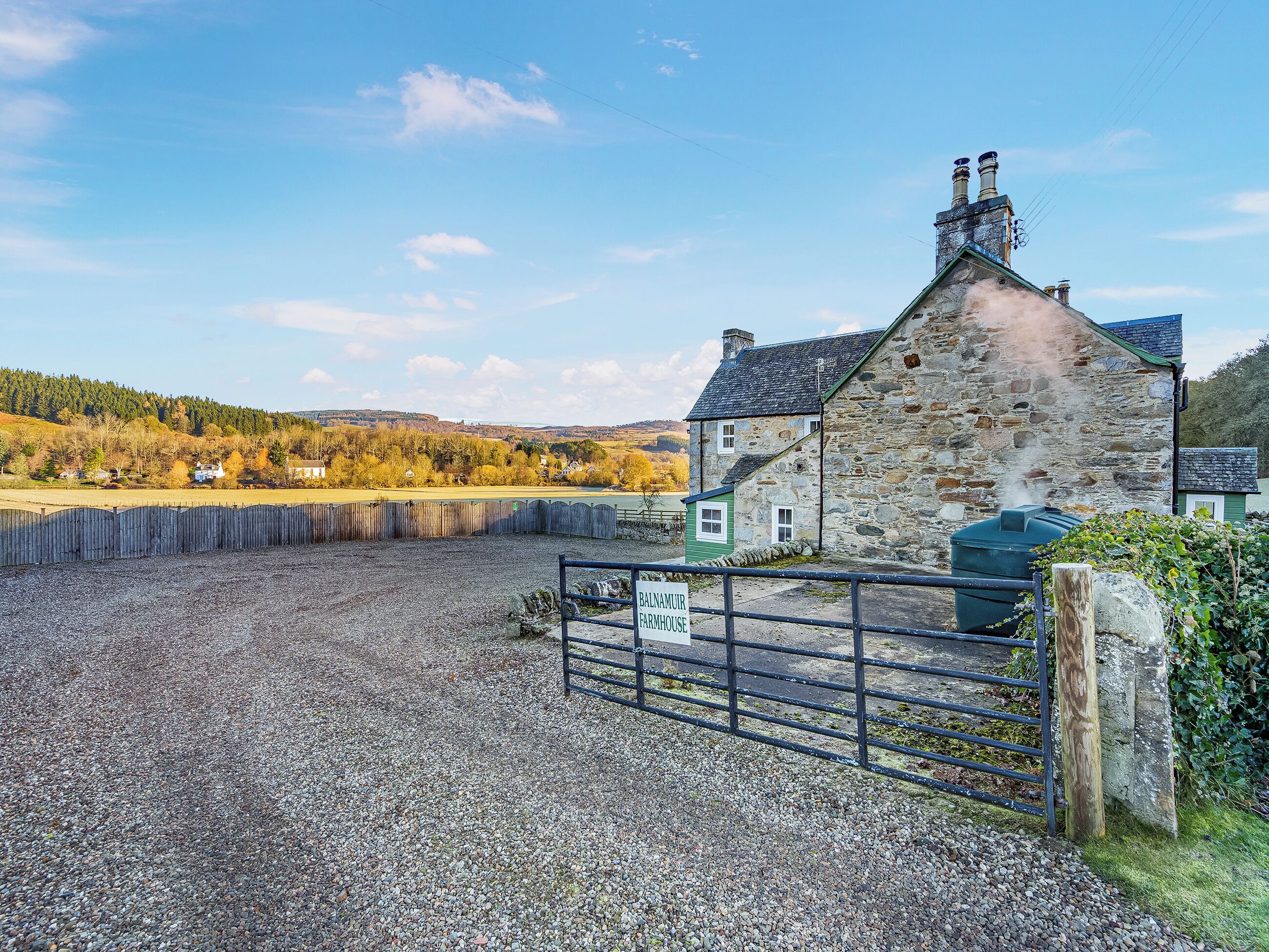 A stone farmhouse with a gravel driveway and a metal gate.