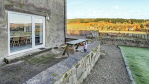 Un edificio de piedra con puerta de cristal, una mesa de madera y vistas a un paisaje campestre.