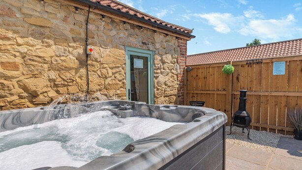 A stone building with a wooden door, a hot tub, and a wooden fence. - 2 bedroom accommodation in Elton, near Stockton-on-Tees (Elton, near Stockton-on-Tees)