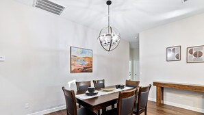 Un comedor con mesa de madera, sillas, una araña y obras de arte en las paredes.