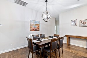 Zona pranzo con tavolo in legno, sedie, un lampadario e opere d'arte alle pareti.