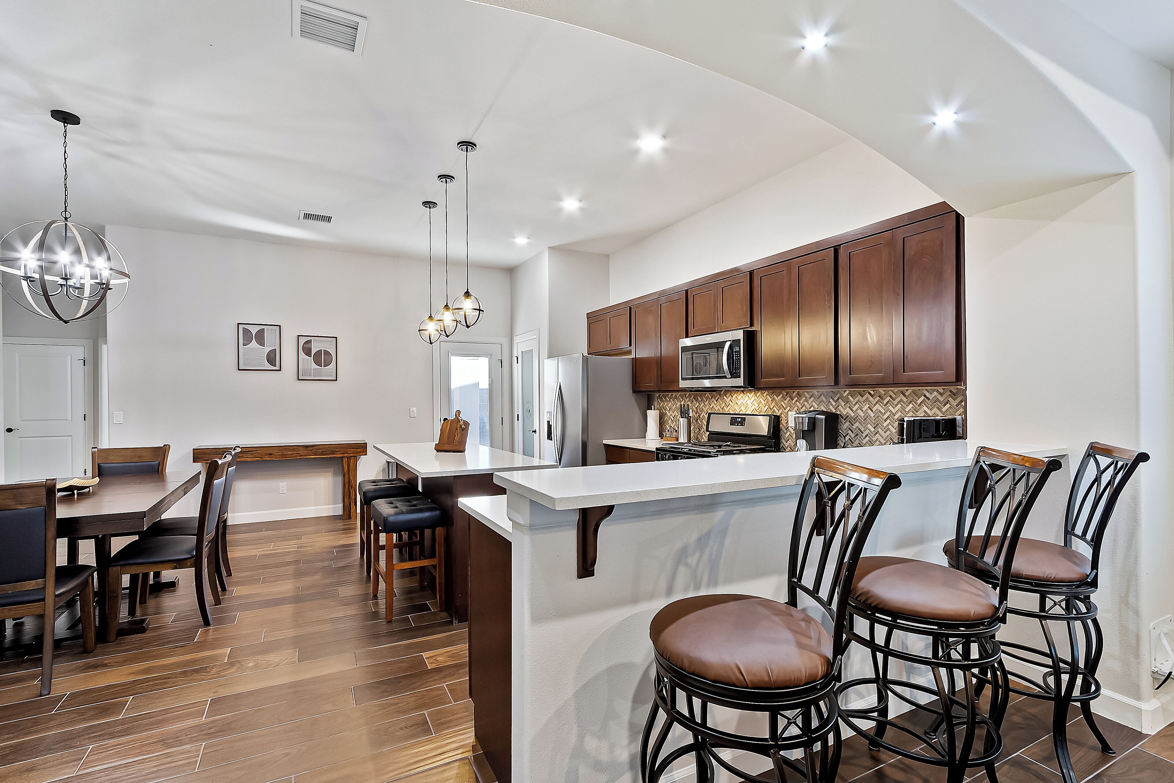 A modern kitchen with wooden cabinets, a central island with bar stools, and pendant lighting.
