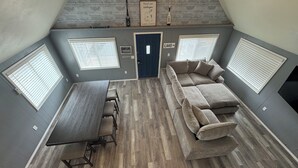 Une pièce de style loft comprenant une table à manger, un canapé et deux fenêtres équipées de stores.