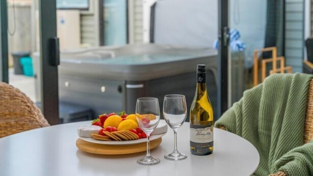 Une table avec une bouteille de vin, deux verres et une assiette de fruits et de crackers.