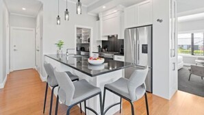 Une cuisine moderne avec des meubles blancs, un îlot central doté de tabourets et un éclairage suspendu.