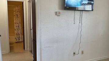 A living room with a flat-screen TV mounted on the wall, a door leading to another room, and a patterned rug on the floor.