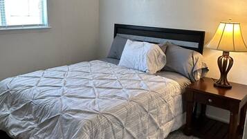 A bedroom with a bed, a ceiling fan, a bedside lamp, and a window with blinds.
