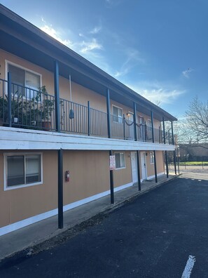 Un motel de dos pisos con techo plano, zona de estacionamiento techada e hidrante en la acera.