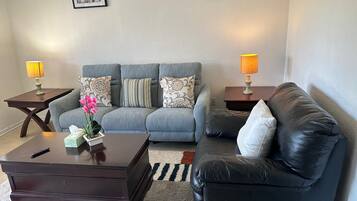 A living room with a grey sofa, a black leather couch, a wooden coffee table, and two side tables with lamps.
