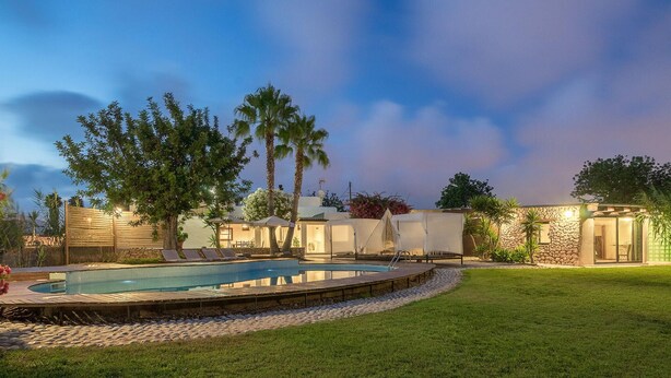 A pool area with a wooden deck, lounge chairs, and a stone wall. - Beach front home in Ibiza (Ibiza)