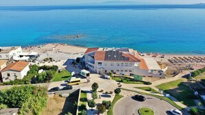 An aerial view of a coastal hotel with a beach, solar panels on the roof, and a parking area. - DOMO 101 - Deluxe Junior Suite with Sea View (Aglientu)