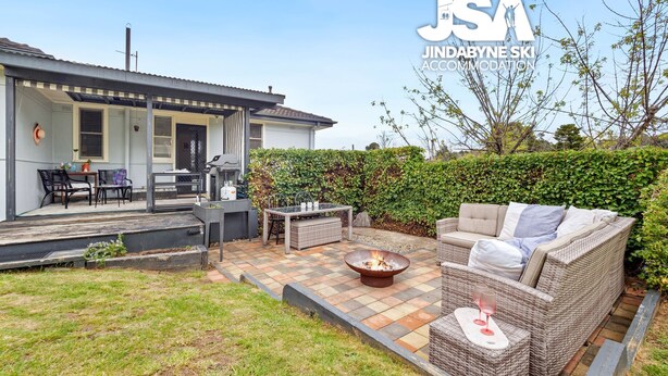 Eine Terrasse mit Feuerstelle, Gartenmöbeln und einer überdachten Sitzgruppe mit Tisch und Stühlen.