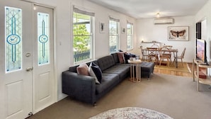 Ein Wohnzimmer mit einem dunkelgrauen Sofa, einem kleinen runden Tisch und einem Essbereich mit Holzsesseln.