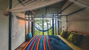 Een kamer met een hangmat, een bed met kleurrijk beddengoed en uitzicht op groen.