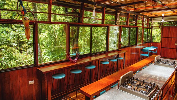 Een bar met houten barstoelen, een lange houten bank en een gasfornuis.