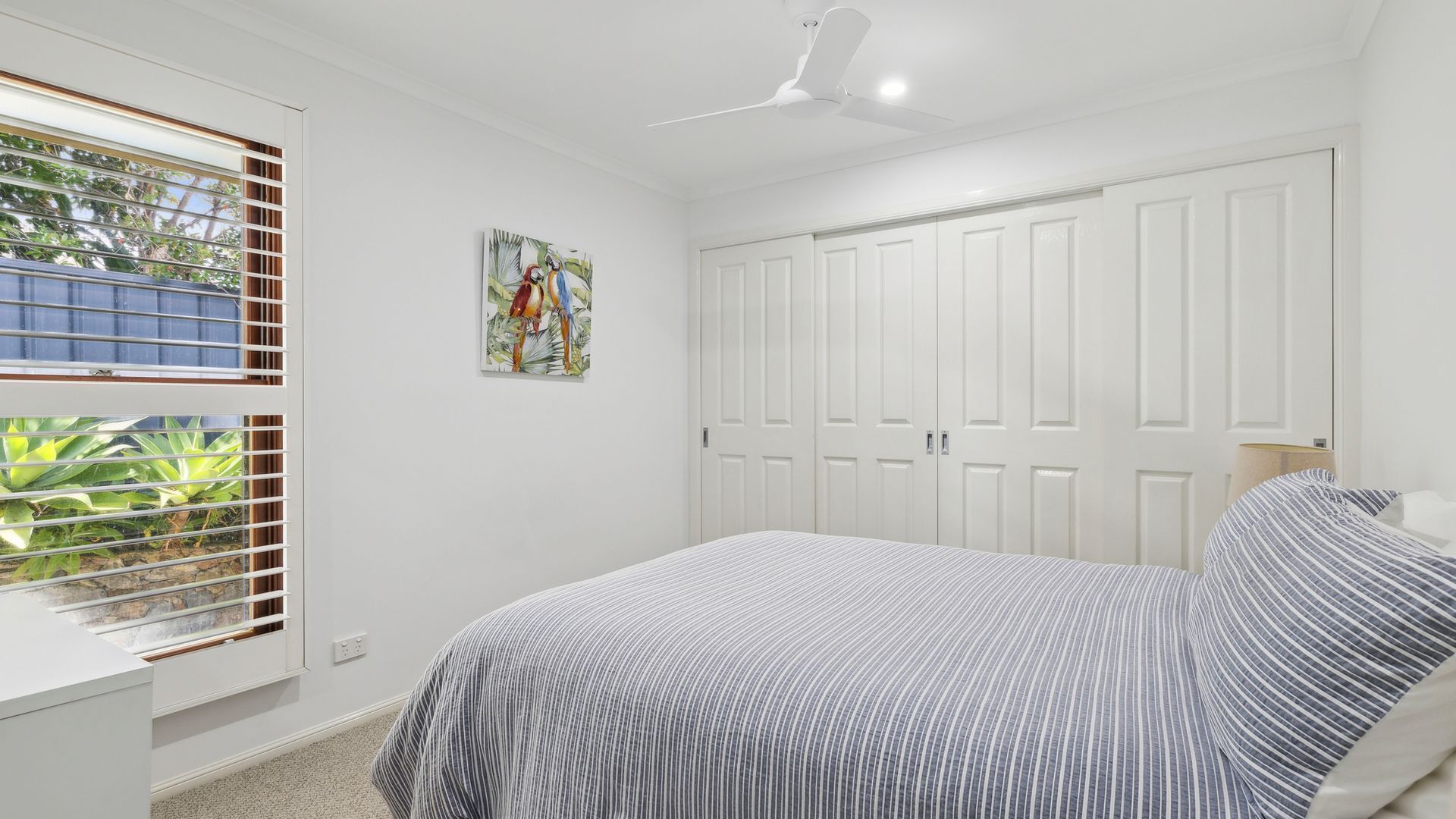 Une chambre à coucher avec un lit, un ventilateur de plafond, une fenêtre avec des stores et une porte.