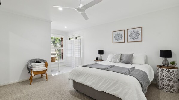 A modern bedroom with a large bed, two bedside tables, a ceiling fan, and a view of the outdoors.