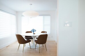 Un coin repas avec une table blanche, quatre chaises marron, un luminaire suspendu blanc et un objet décoratif bleu.
