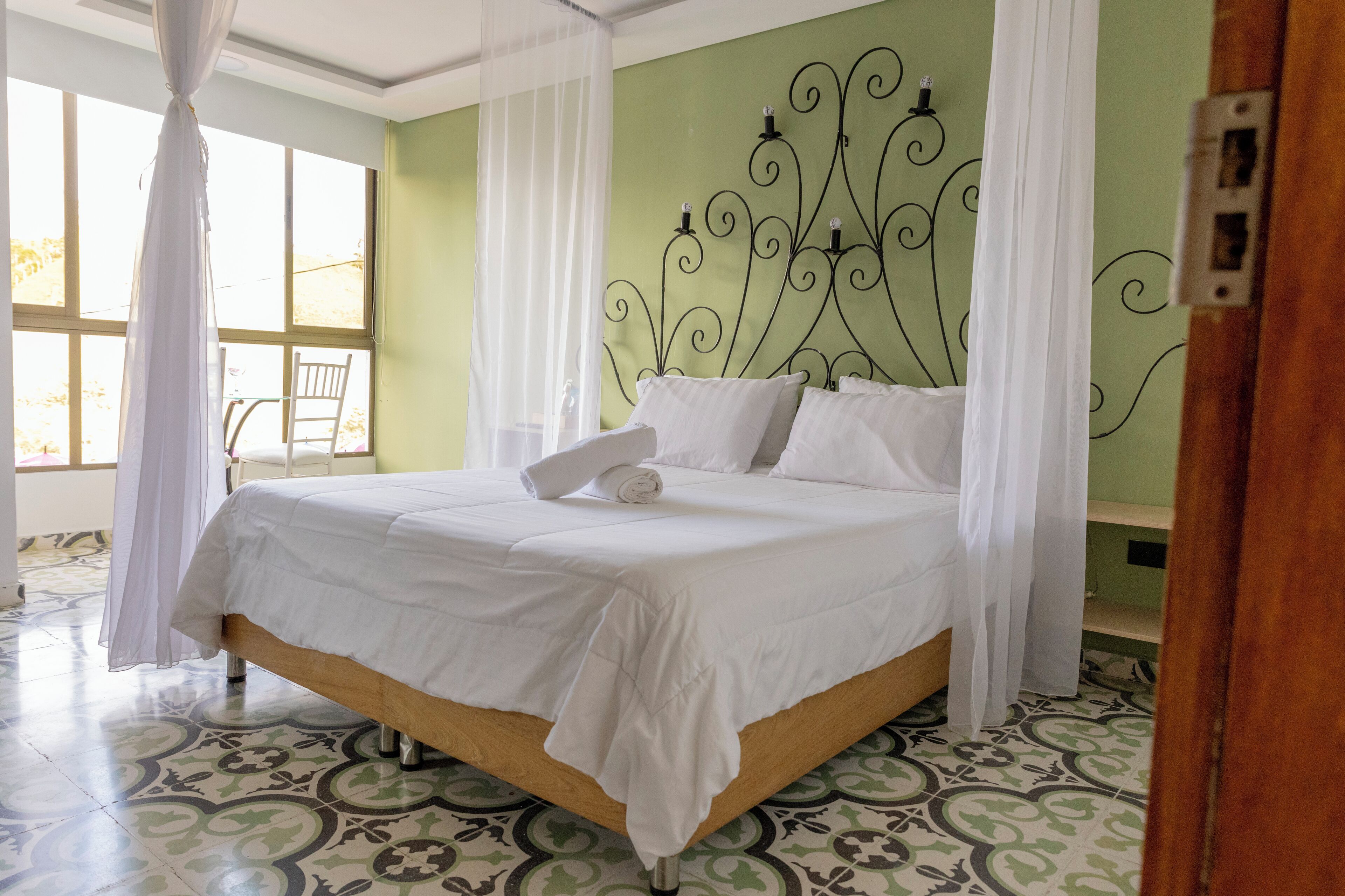 A neatly made bed with white linens, a headboard with a decorative metal design, and a patterned floor.
