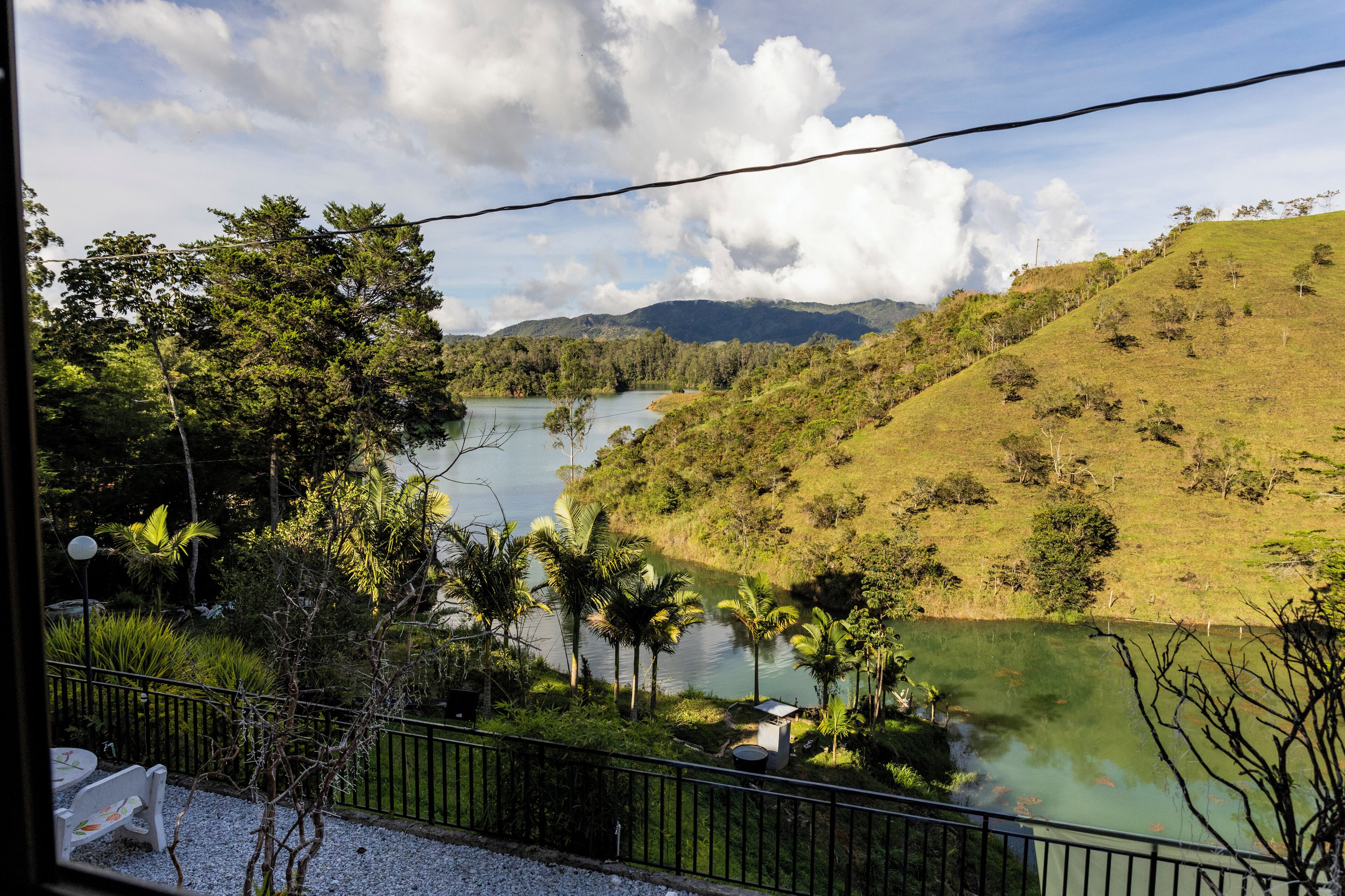 A view of a lake surrounded by lush greenery and hills, with a clear sky above.
