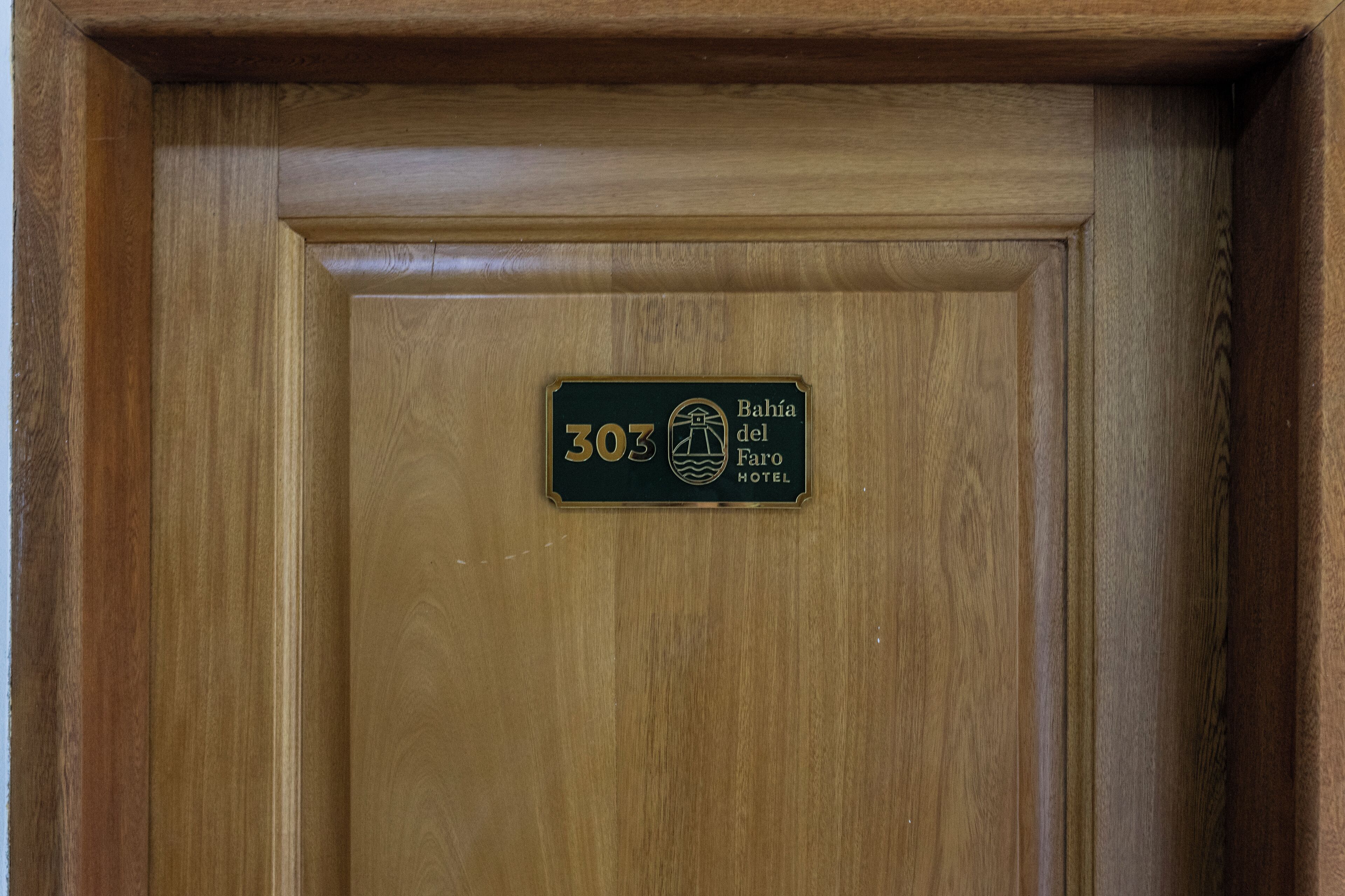 Eine Holztür mit einem Schild, das Raum Nummer 303 des Hotels Bahía del Faro angibt.
