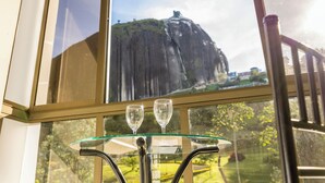 A table with two glasses and a view of a mountain through a window. - Hotel Bahía Del Faro (Guatapé)