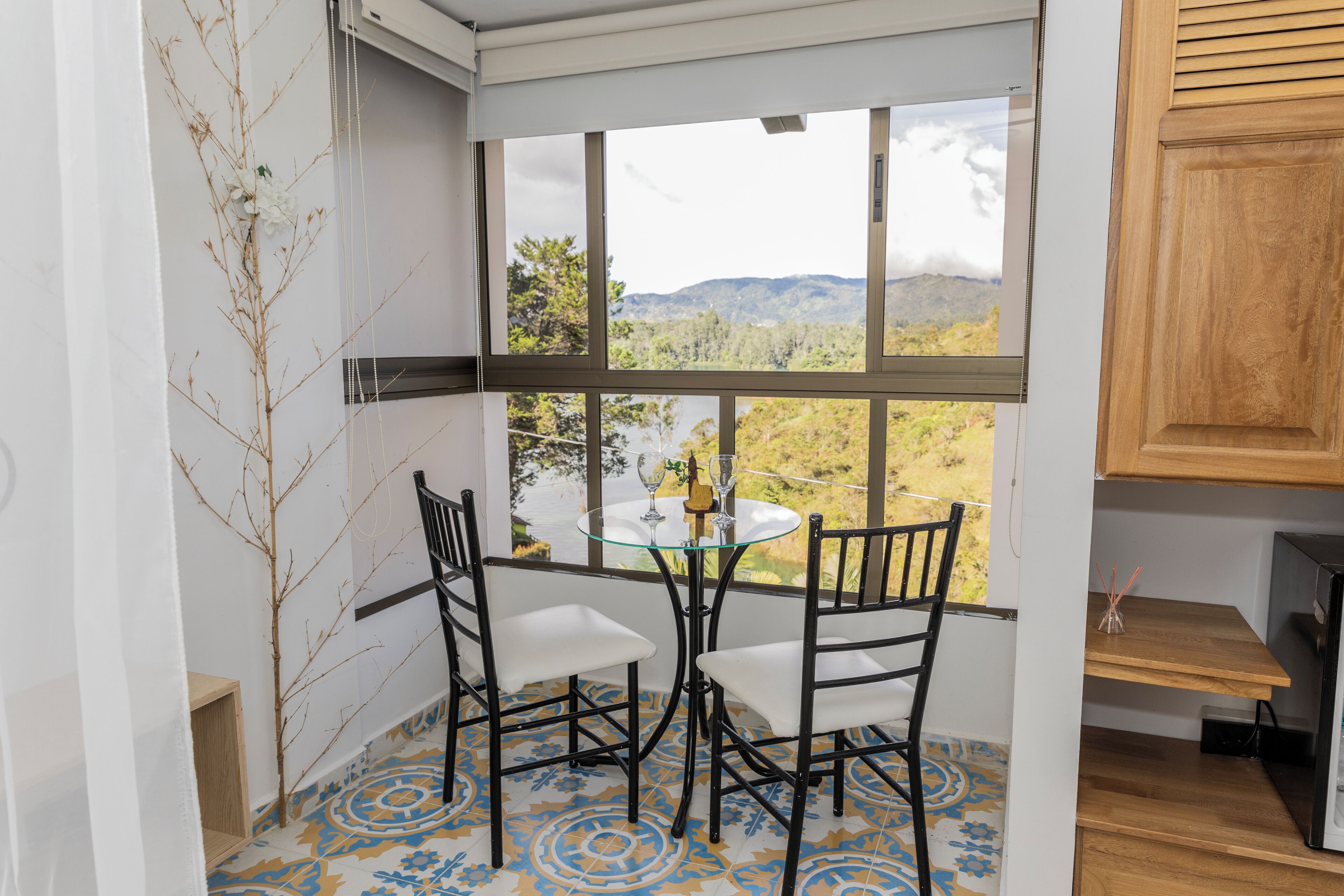 Una habitación de esquina con una mesa y sillas de vidrio, vistas a un paisaje montañoso y un armario de madera.