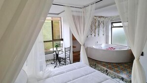 A bedroom with a large bed, a sitting area with a table and chairs, and a bathroom with a bathtub. - Hotel Bahía Del Faro (Guatapé)
