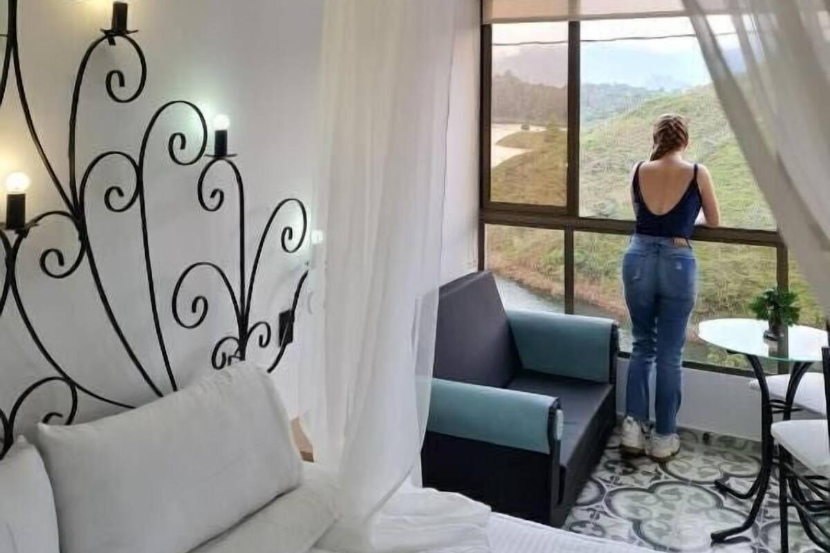 Un dormitorio con un ventanal grande, una cama, un sofá y una pequeña mesa.