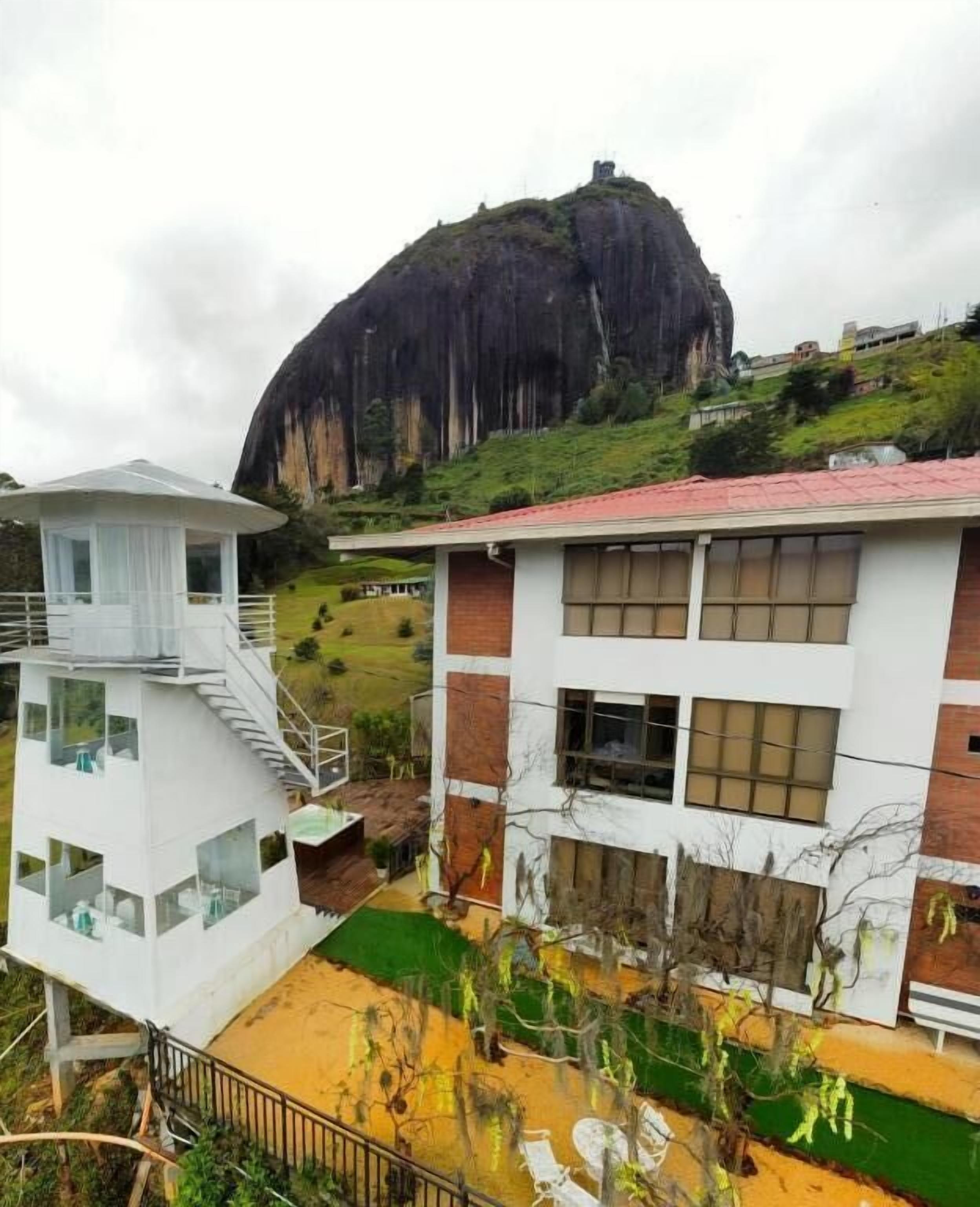 A building with a white exterior and a red roof, adjacent to a large rock formation.