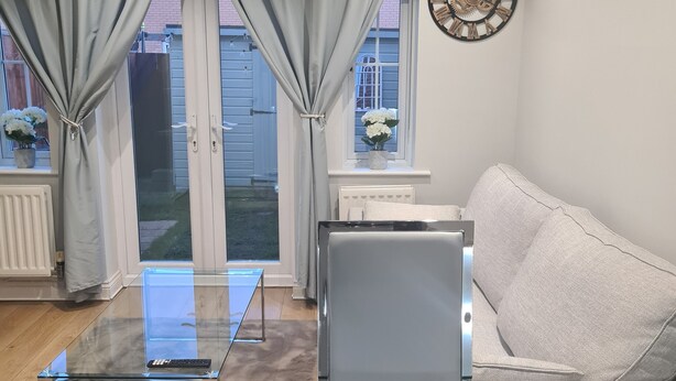 A modern living room with a glass coffee table, a grey sofa, and a decorative clock on the wall. - Entire house 🏠.  suitable for families and workers.  (Middlesbrough)