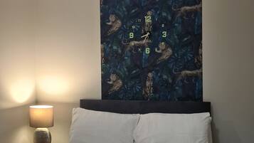 A bedroom with a bed, a nightstand, a lamp, and a wall clock with a jungle-themed design.