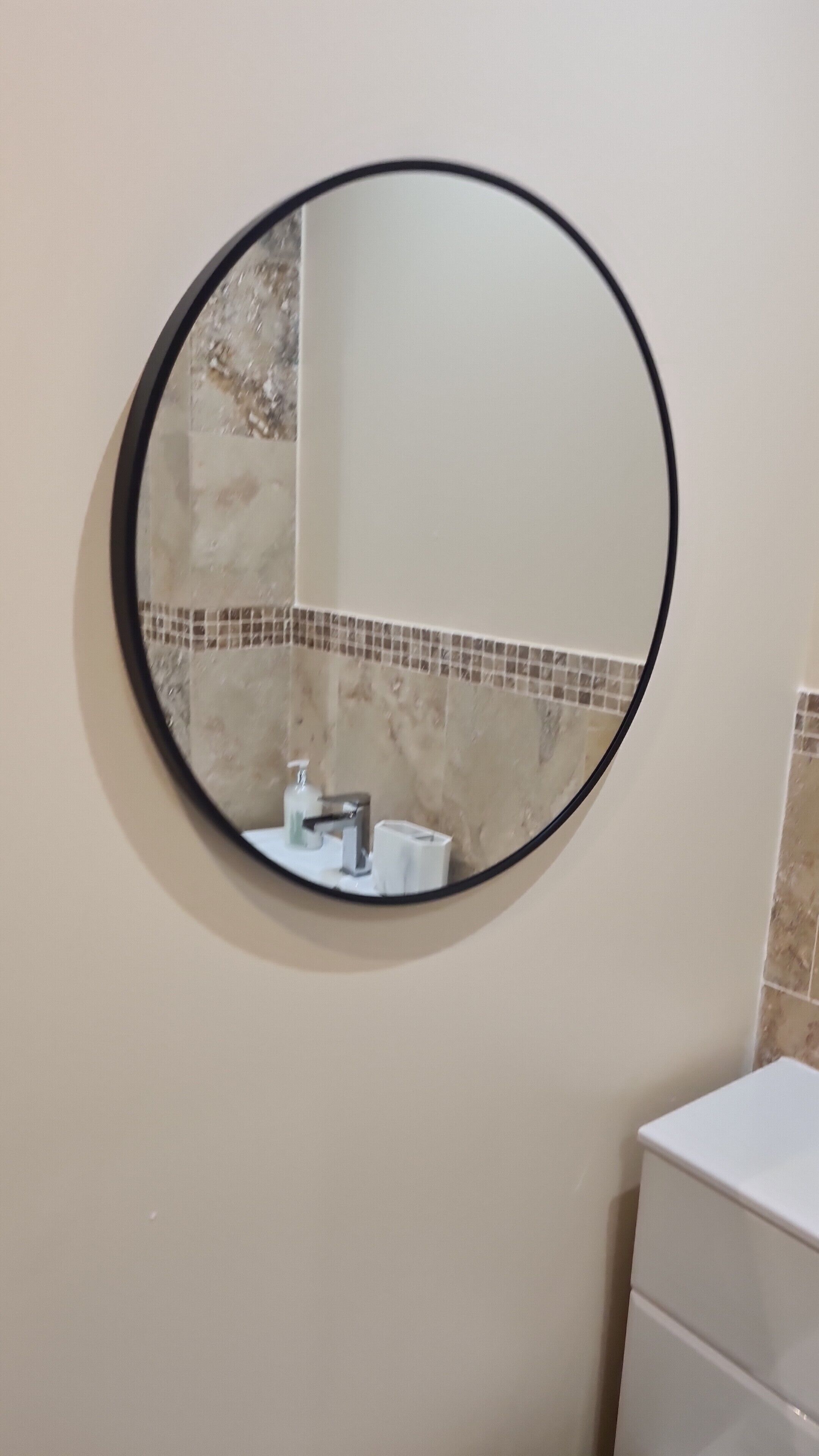 Un miroir rond, doté d’un cadre noir, fixé au mur.