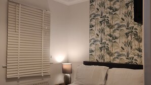 A bedroom with a bed, a nightstand, a lamp, a window with blinds, and a wall with a tropical wallpaper. - Entire house 🏠.  suitable for families and workers.  (Middlesbrough)