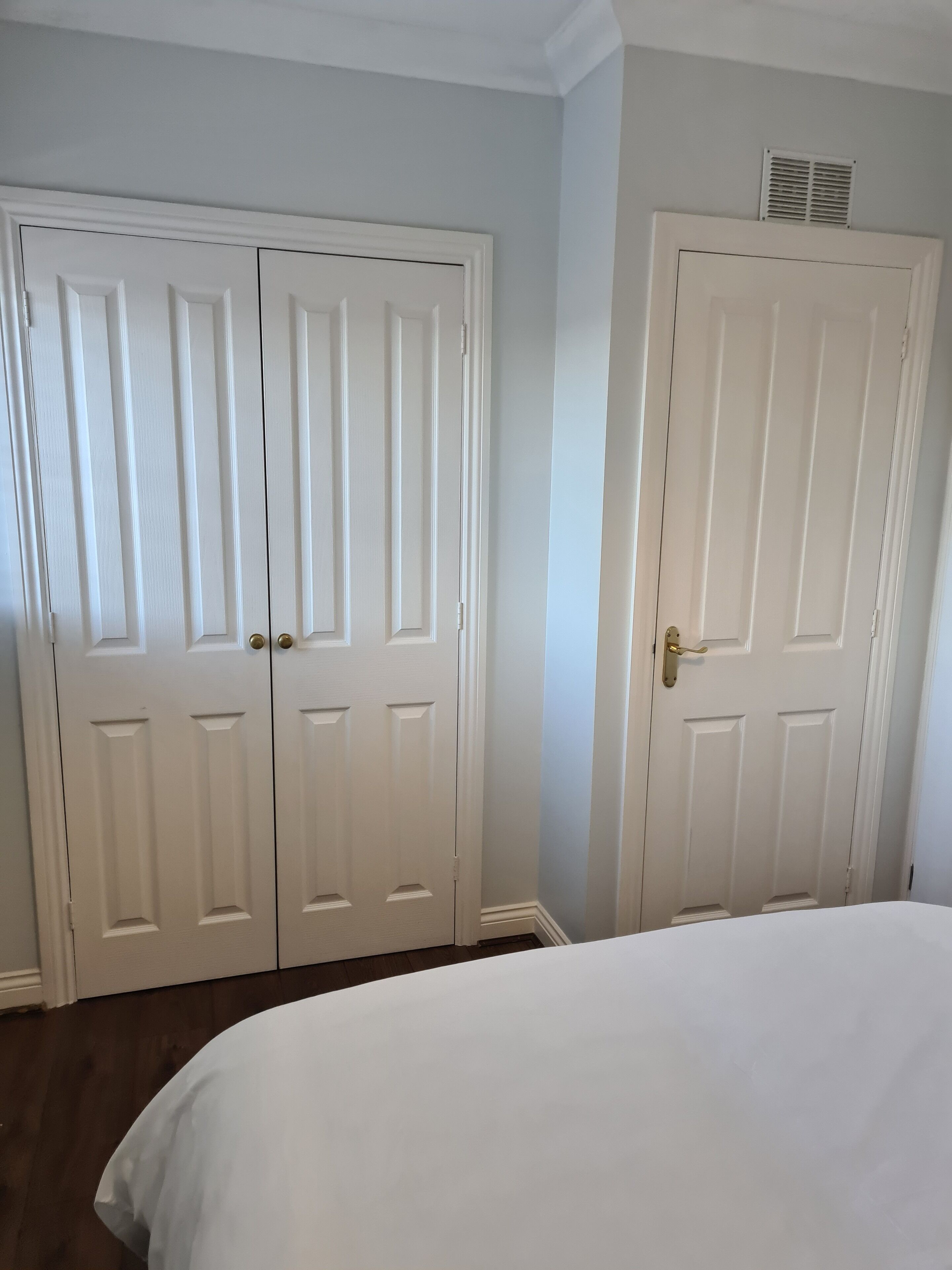 Un dormitorio con dos puertas blancas, una cama y una rejilla en la pared.