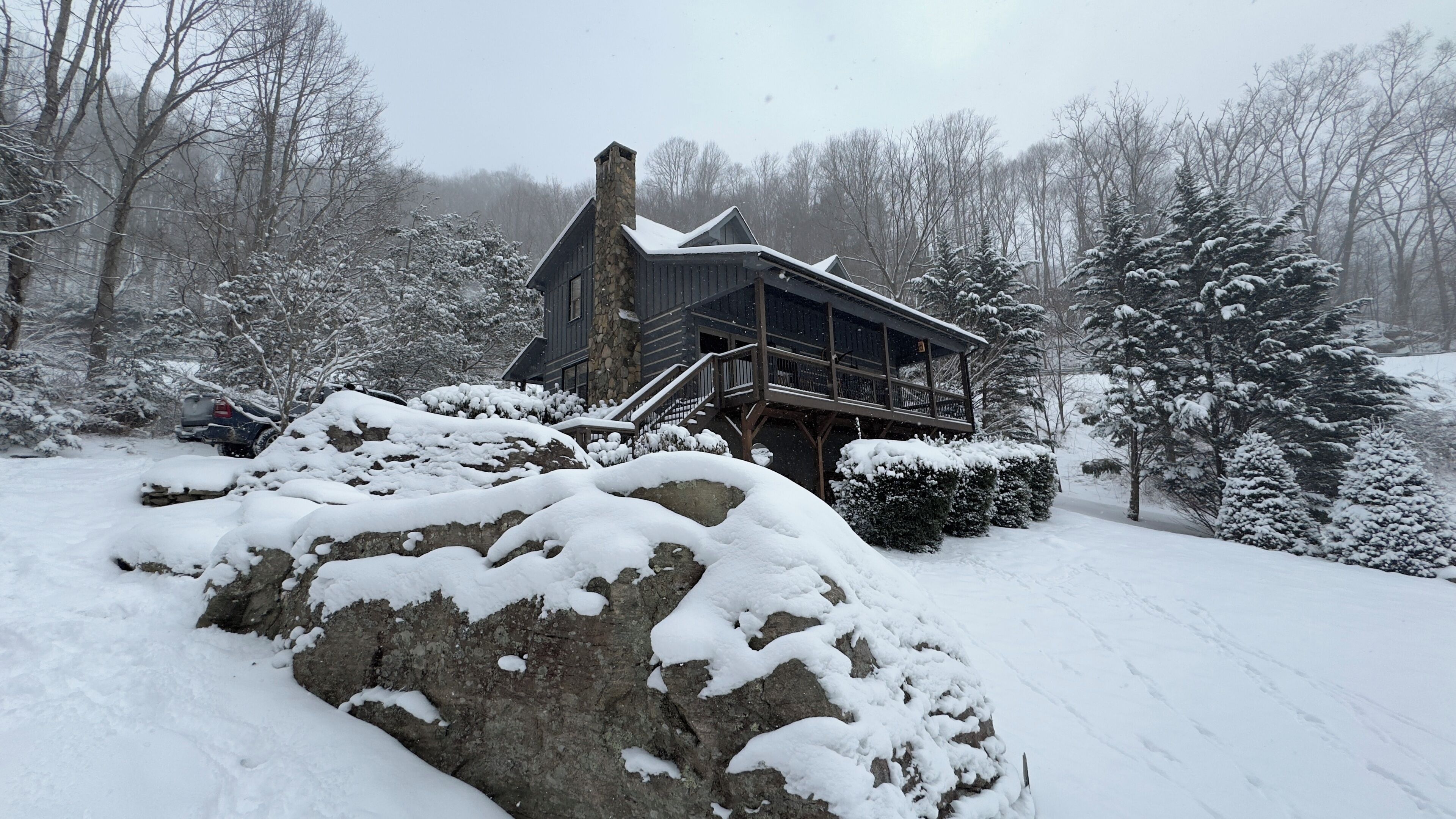 A cabin with a stone chimney, wooden deck, and snow-covered surroundings.
