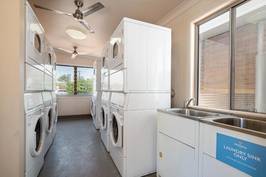A laundry room with multiple washing machines, a ceiling fan, and a sink marked for laundry use only.
