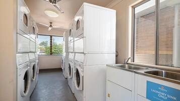 A laundry room with multiple washing machines, a ceiling fan, and a sink marked for laundry use only.