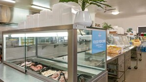 A food service area with a glass display case containing various food items, a sign indicating 'FOOD FOR CRIB', and a plant on top of the display case. - Discovery Parks - Cloncurry (Cloncurry)
