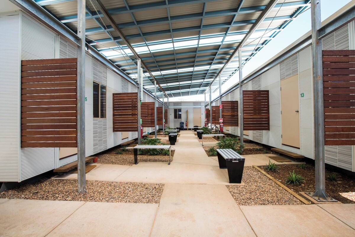 A covered outdoor corridor with rows of mobile homes, each with a door number.