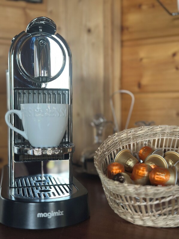 A coffee machine with a cup holder and a basket of coffee capsules on a wooden table.
