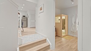 A modern interior with a staircase leading to a kitchen, a wooden cabinet, and a white robe hanging on the wall. - 2BR Apt + Sauna in Earth House, Minutes to Boulder (Superior)