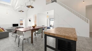 Amplia sala de estar con una mesa de comedor de madera, un sofá gris y una escalera que sube a un nivel superior.