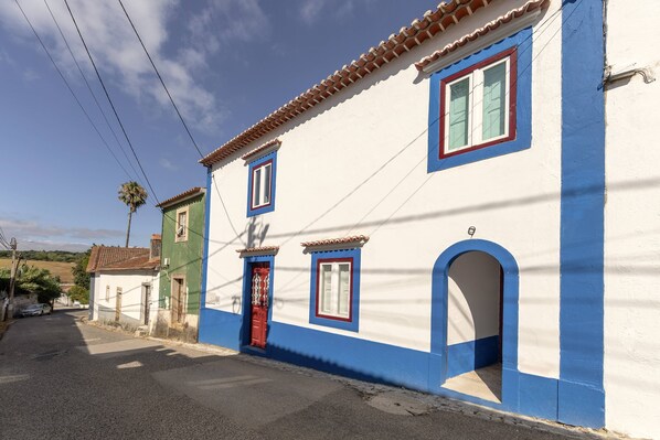 A narrow street with a white building with blue trim and a red door.