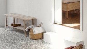 Una habitación con una cama, un banco de madera, una mesita pequeña y un perchero en la pared.