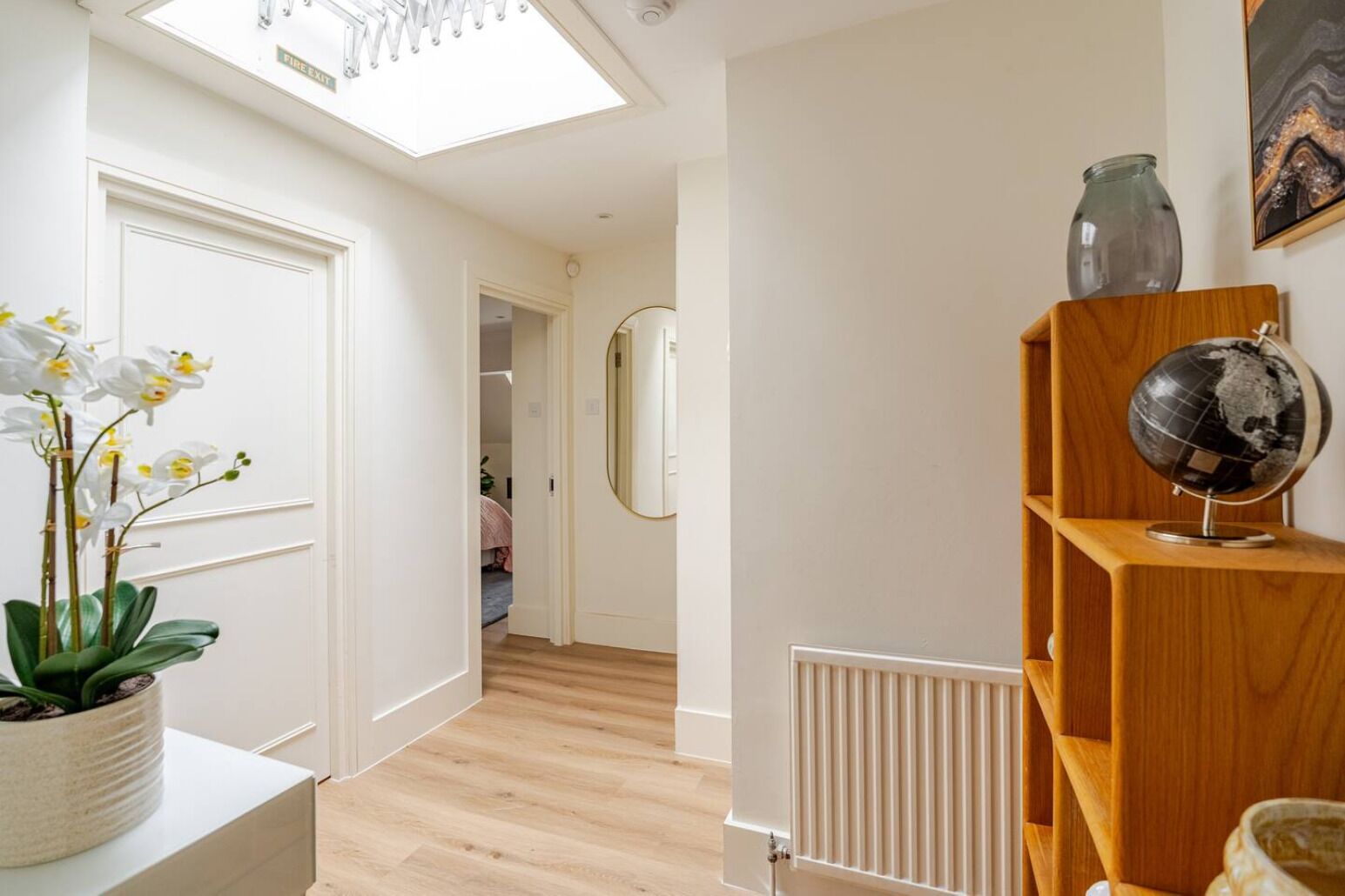 A hallway with a skylight, a potted orchid, a globe on a wooden shelf, and a radiator.
