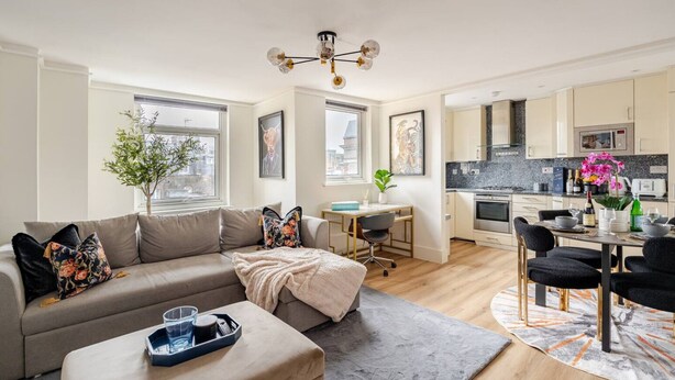 Een modern appartement met een woonkamer, eethoek en keuken. Het heeft een bank, een eettafel met stoelen, een keuken met apparatuur en een hanglamp.